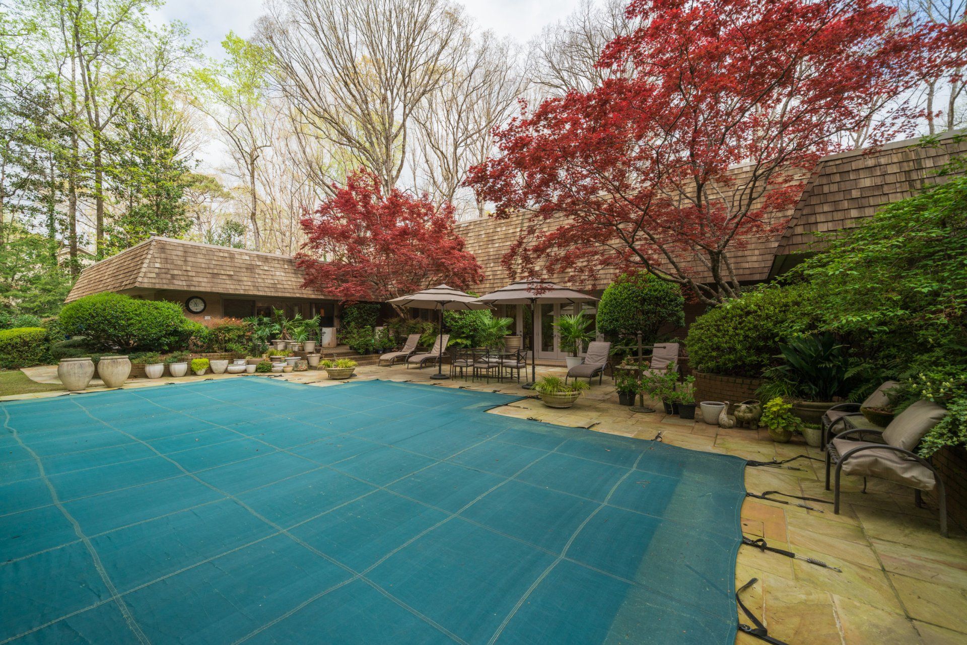 A large swimming pool with a blue cover in the backyard of a house.