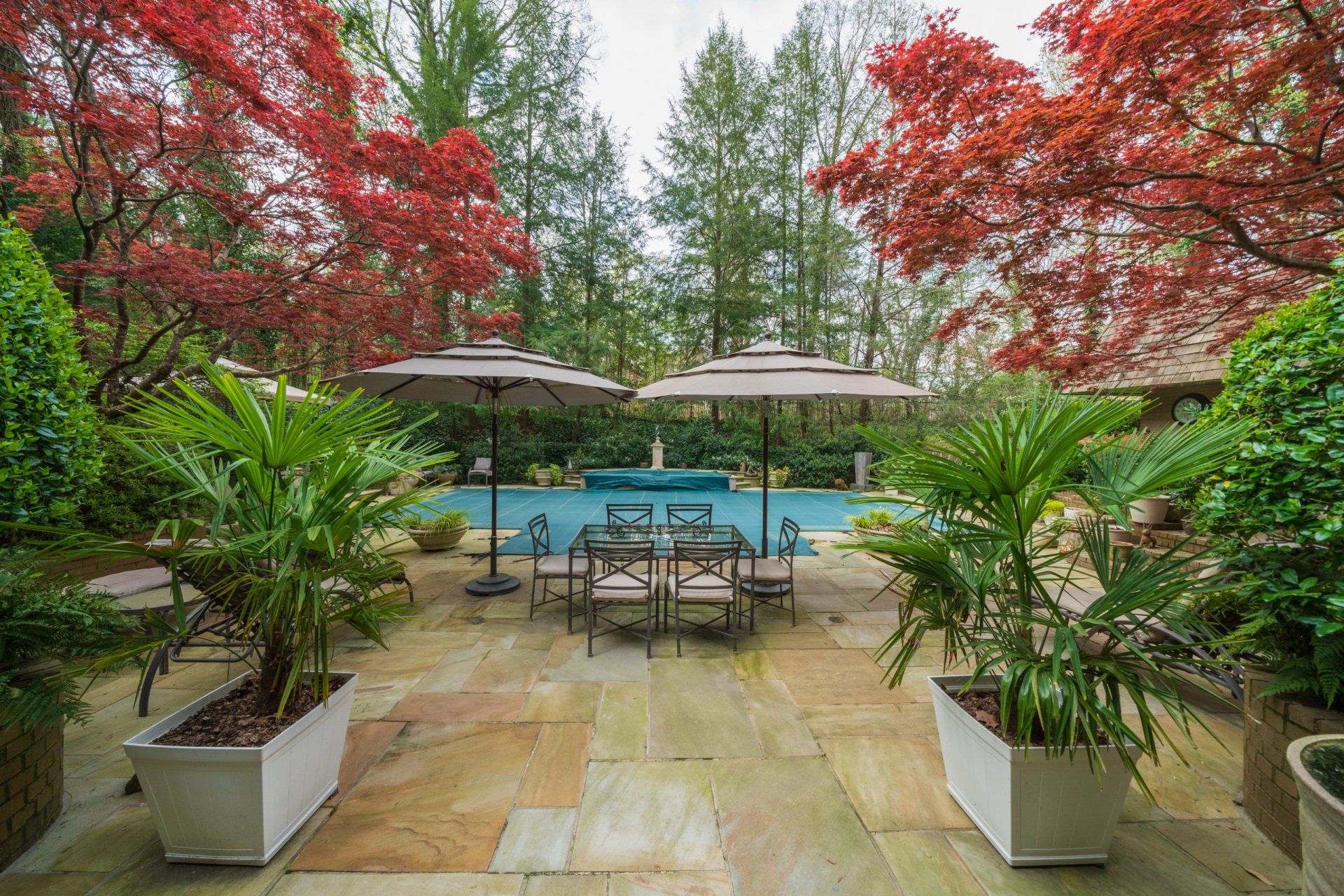 A patio with a table and chairs and umbrellas in front of a pool.