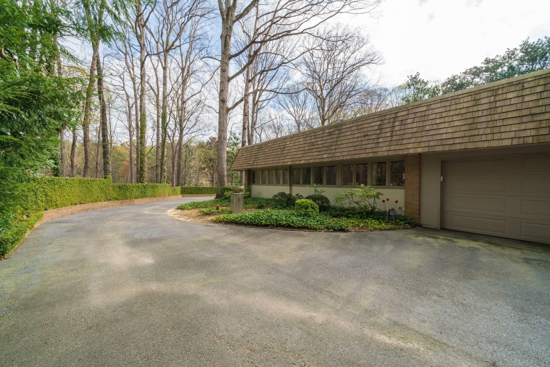 A house with a garage and a driveway leading to it surrounded by trees.