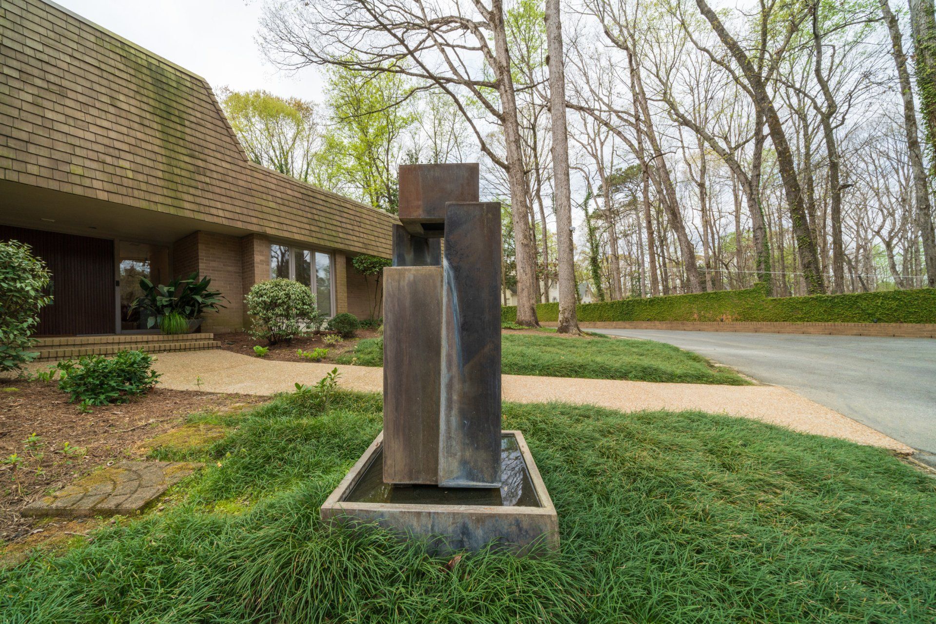 A sculpture in front of a house with trees in the background.
