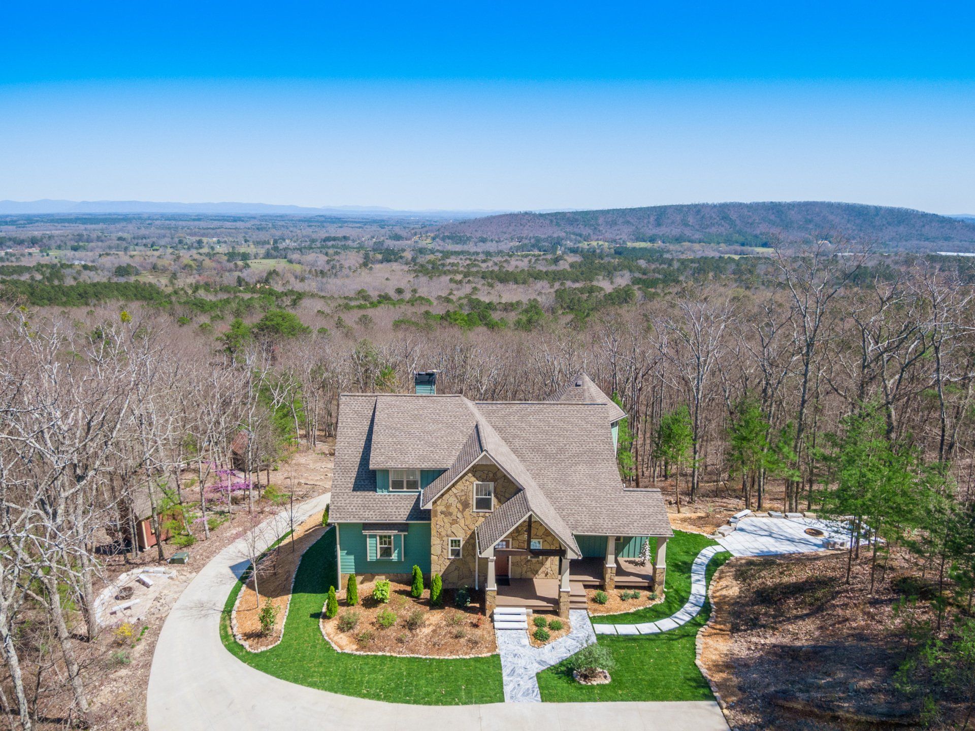 An aerial view of a house on top of a hill in the middle of a forest.