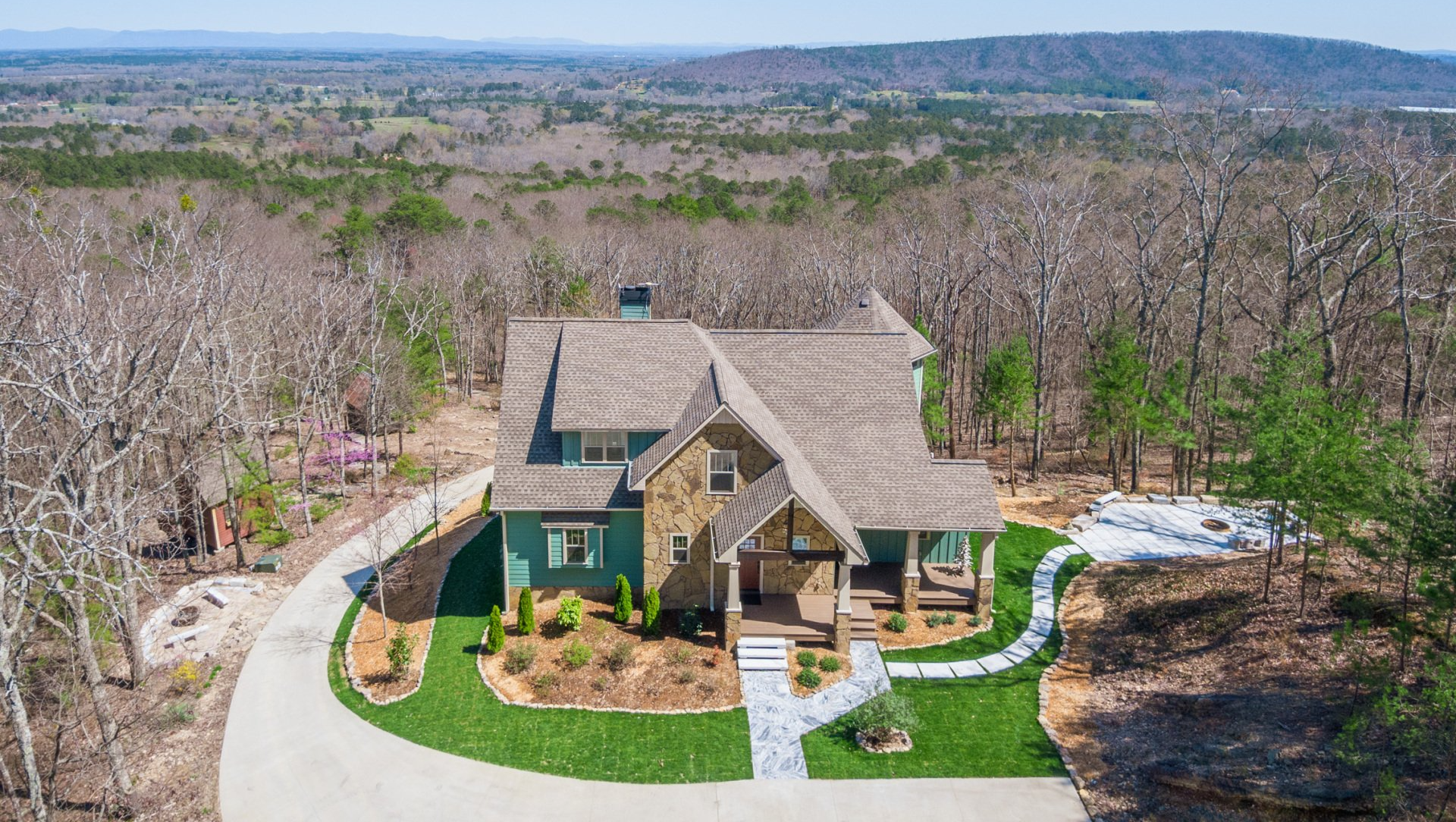 An aerial view of a large house sitting on top of a hill in the middle of a forest.