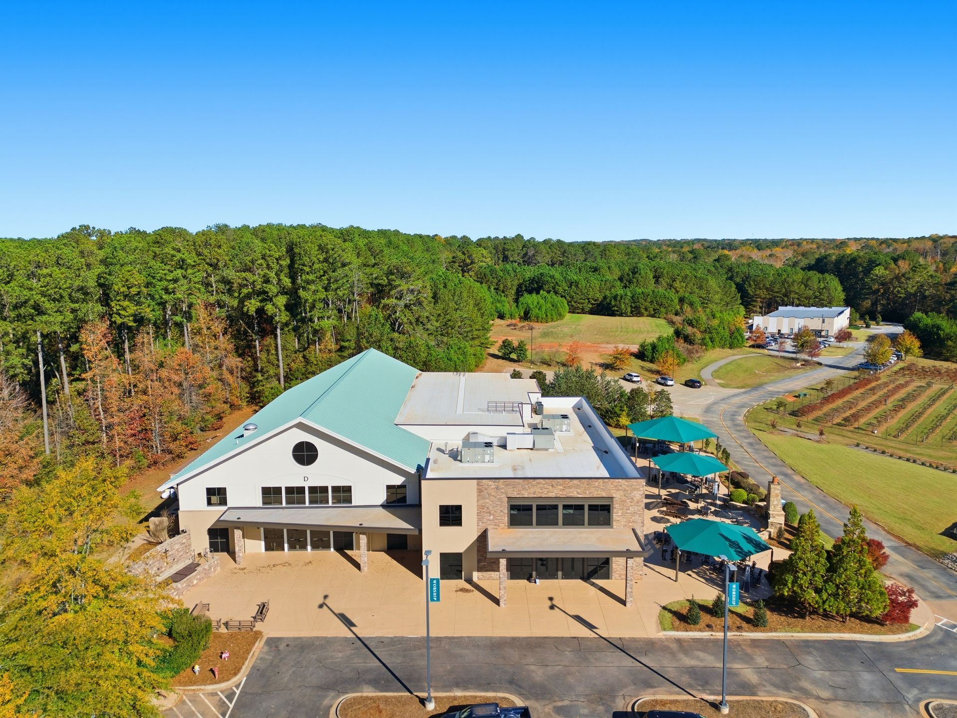 An aerial view of a winery building with a green roof, patio, and vineyards, in front of a forest.