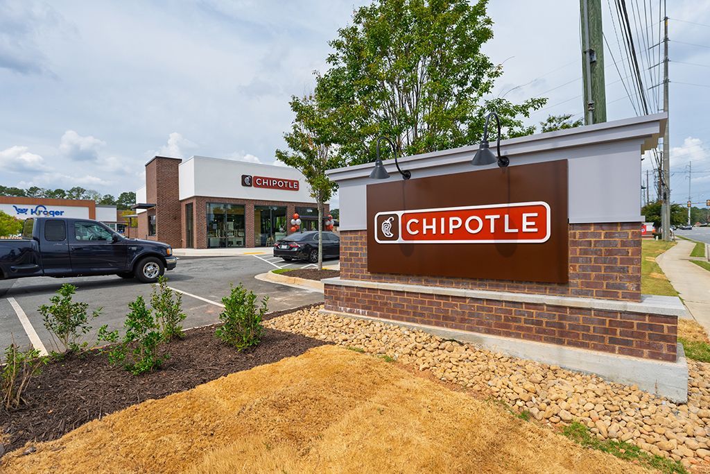 Chipotle restaurant exterior with sign, brick details, parking lot, and a black pickup truck. Cloudy sky.