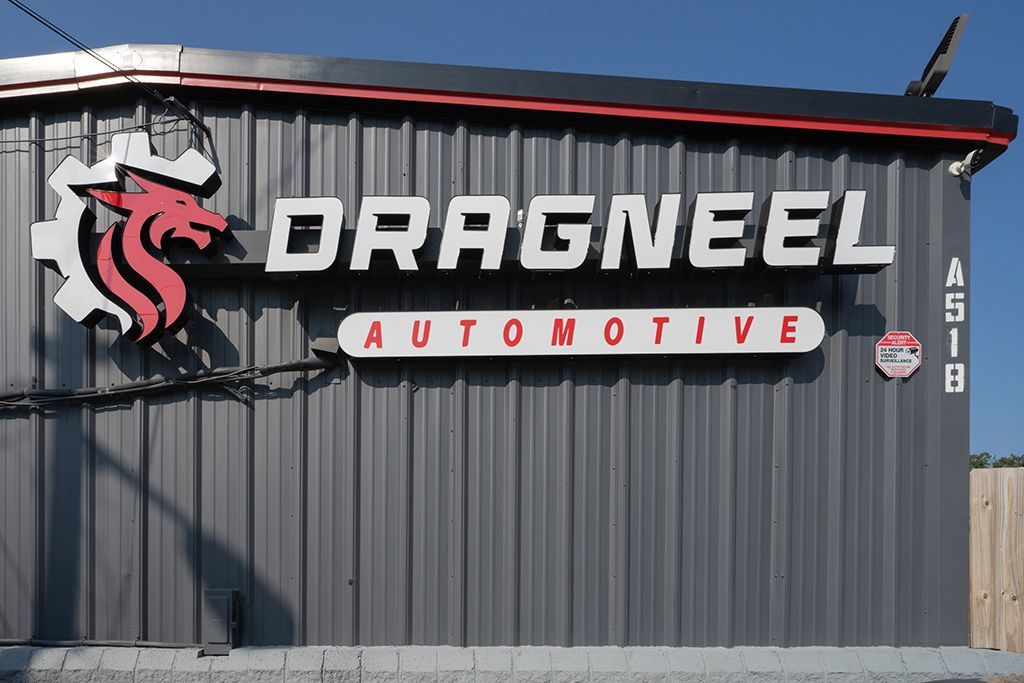 Sign for Dragneel Automotive, featuring a red and white dragon logo and white text on a corrugated metal building.