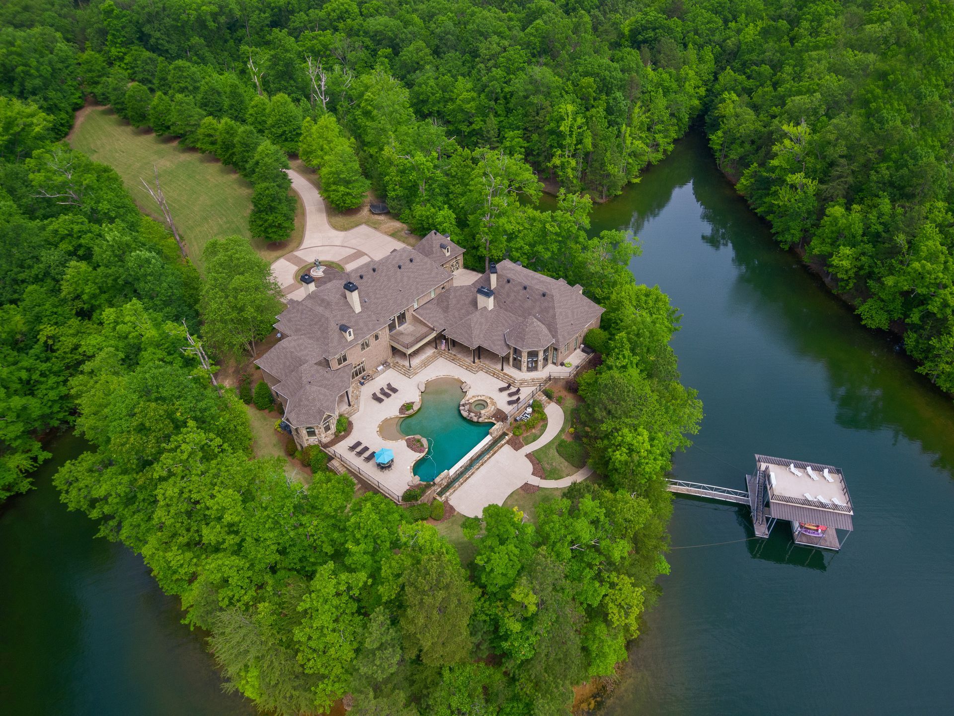 Luxury home on lake, surrounded by green trees, with a pool and dock.