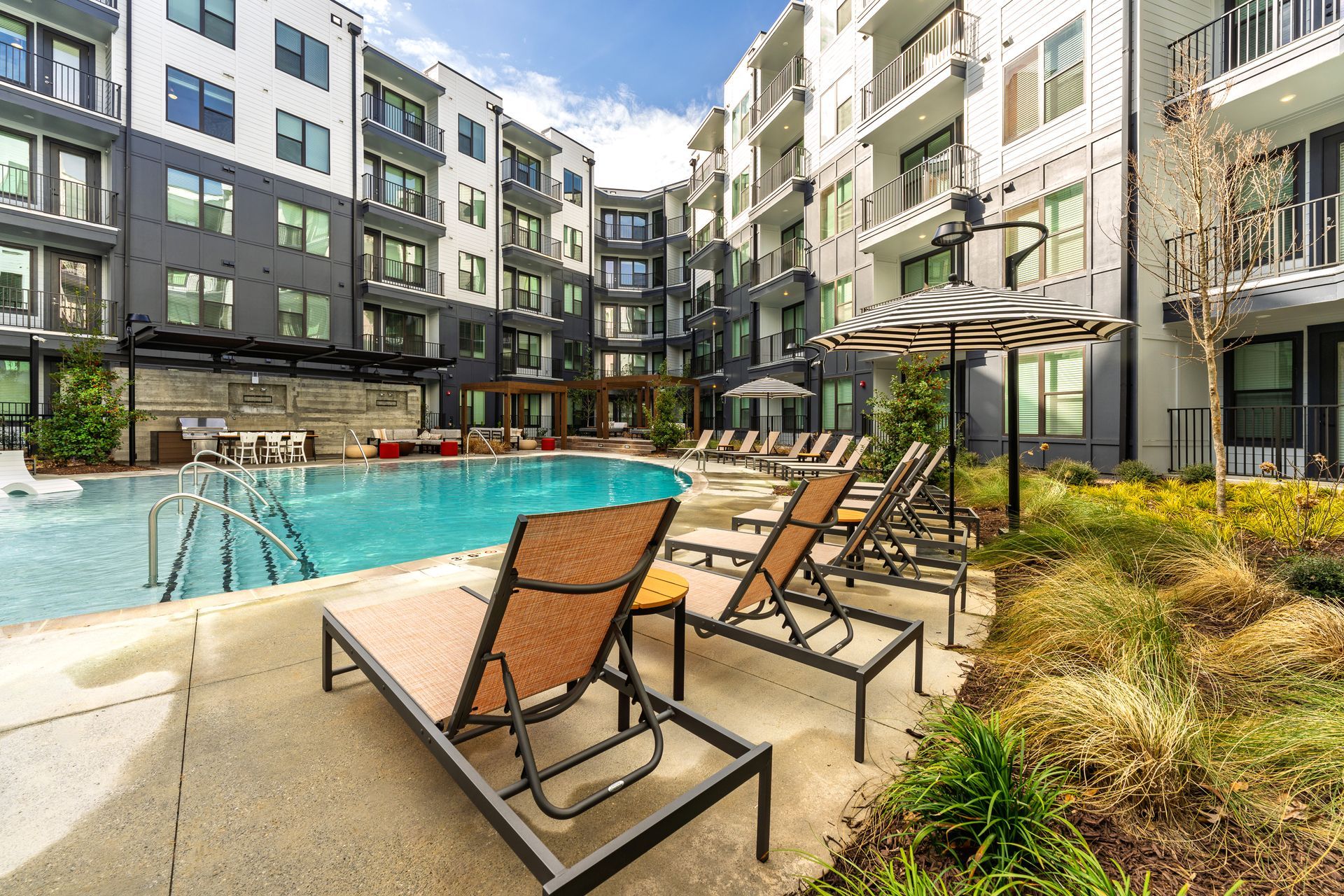 Apartment complex courtyard with a pool, lounge chairs, and buildings.