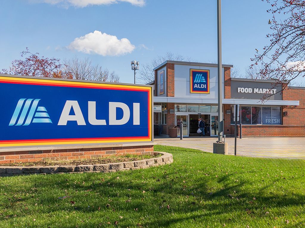 ALDI grocery store entrance with blue sign, brick building, and green lawn on a sunny day.