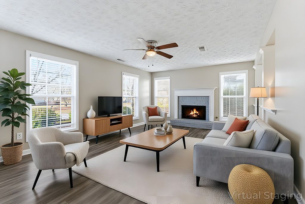 Living room with fireplace, windows, gray sofa, wooden coffee table, and large potted plant.