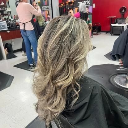Woman with wavy, highlighted hair in a salon chair, hair cape on.