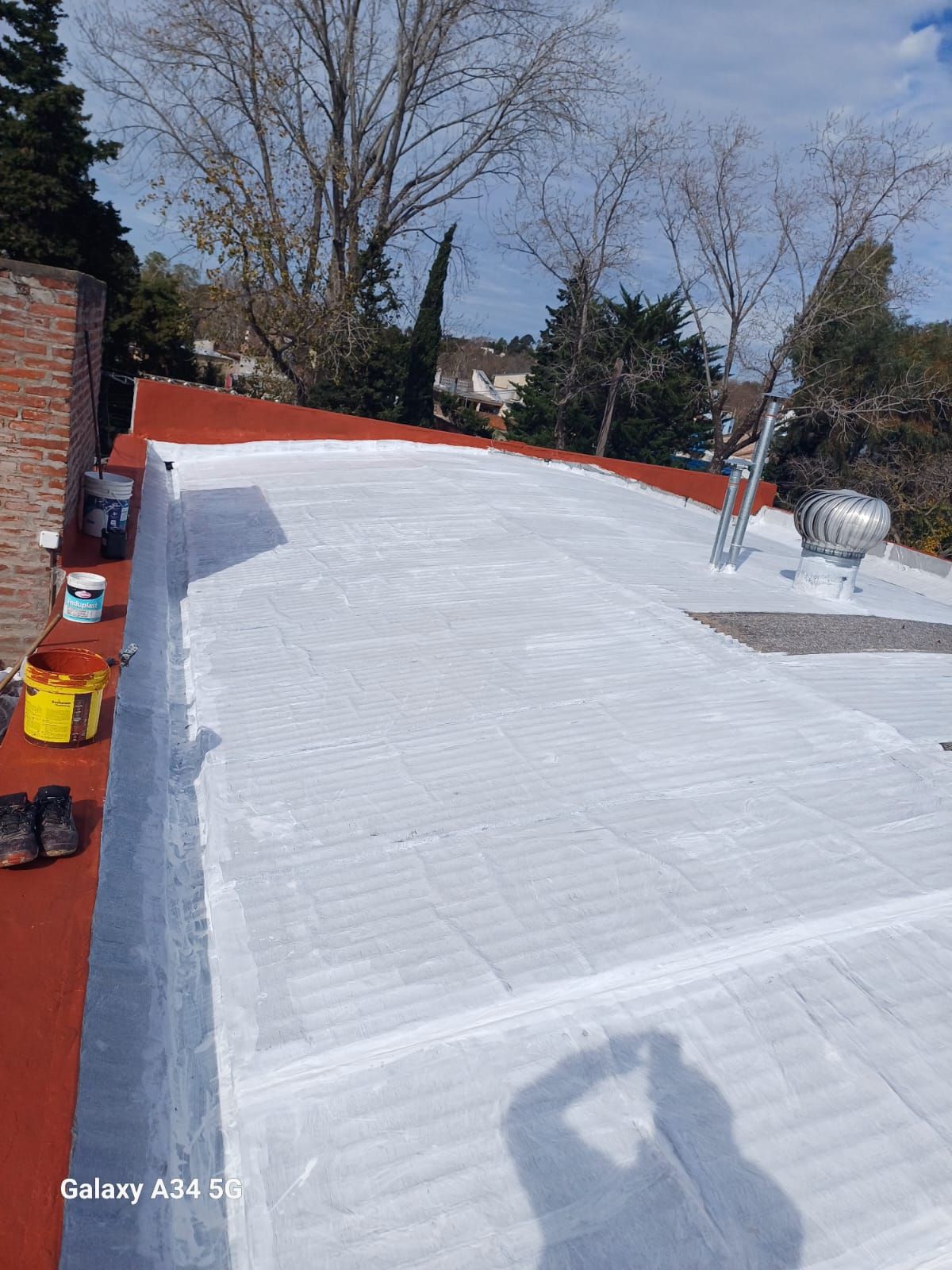 Azotea plana revestida de blanco con rejillas de ventilación y un parapeto de ladrillo,