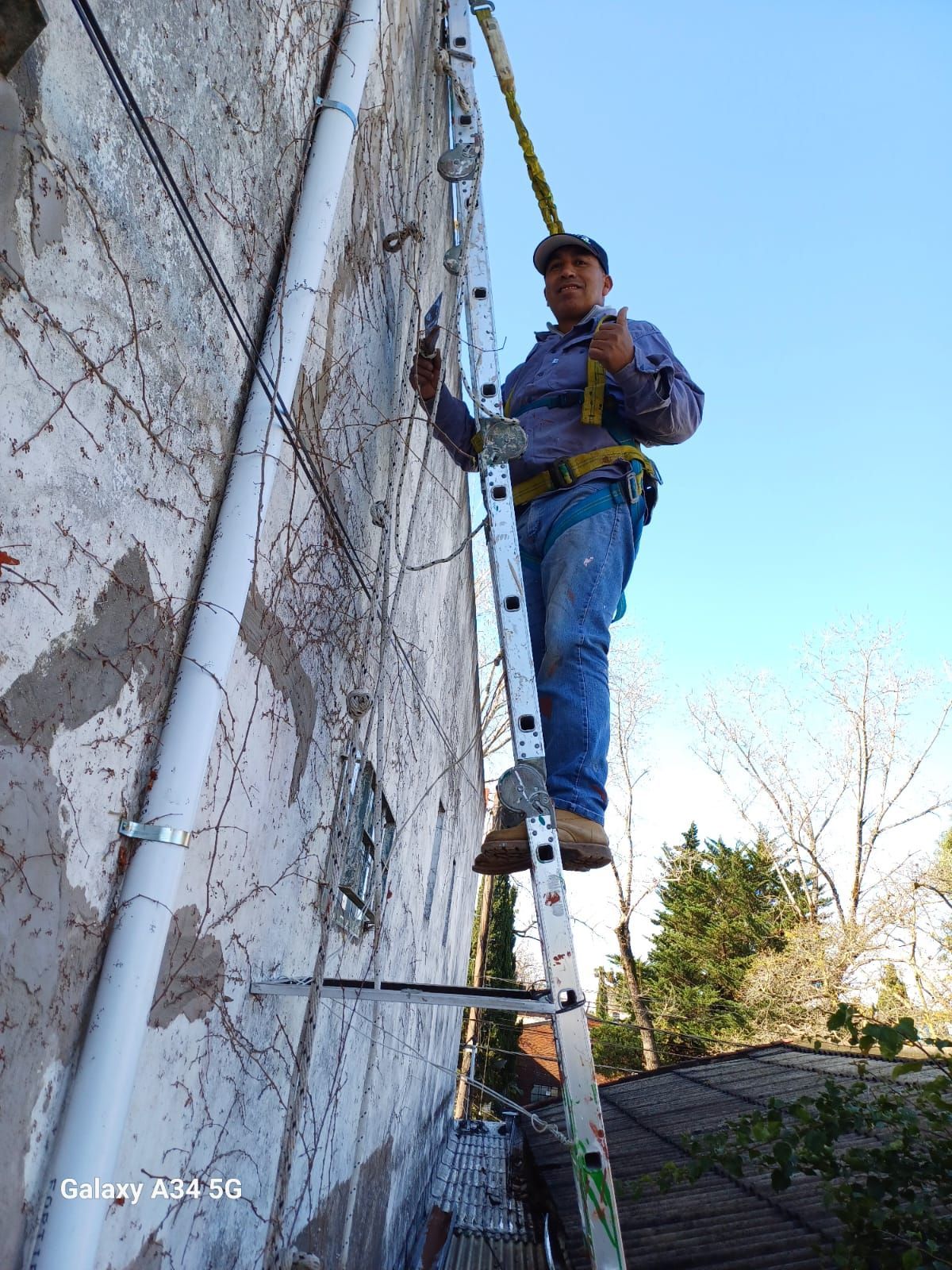 Un trabajador subido a una escalera pinta una pared al aire libre junto a una tubería alta.