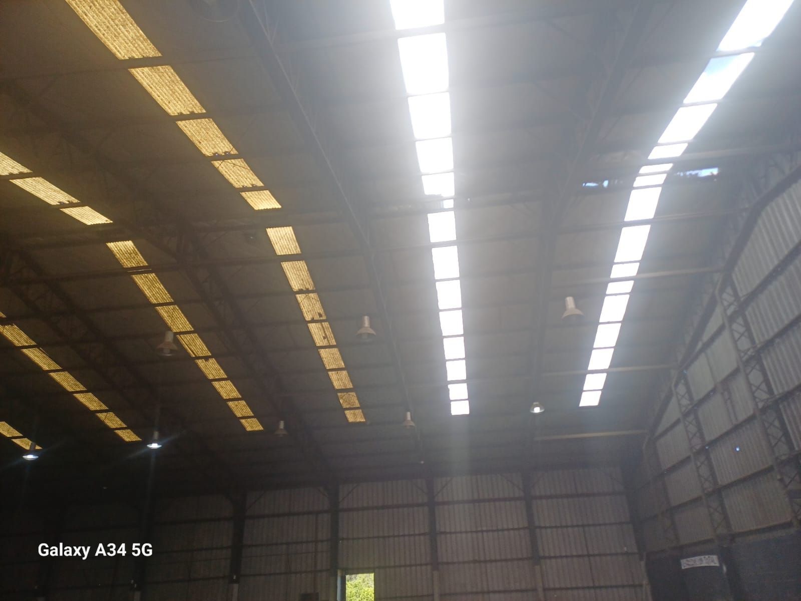 Interior de un almacén con luces en el techo y paredes metálicas, visto desde abajo hacia arriba.