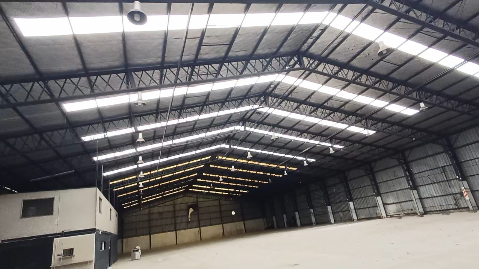Interior vacío de un gran almacén con un alto techo metálico y claraboyas luminosas.