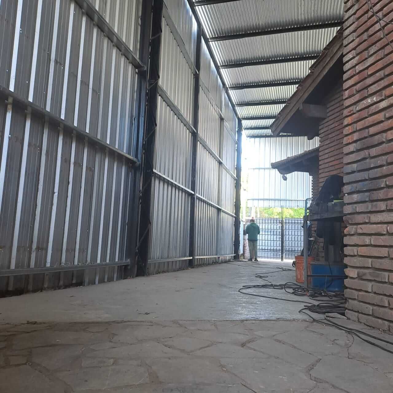 Pasillo industrial cubierto con paredes de chapa ondulada, lateral de ladrillo y una persona cerca del extremo más alejado,