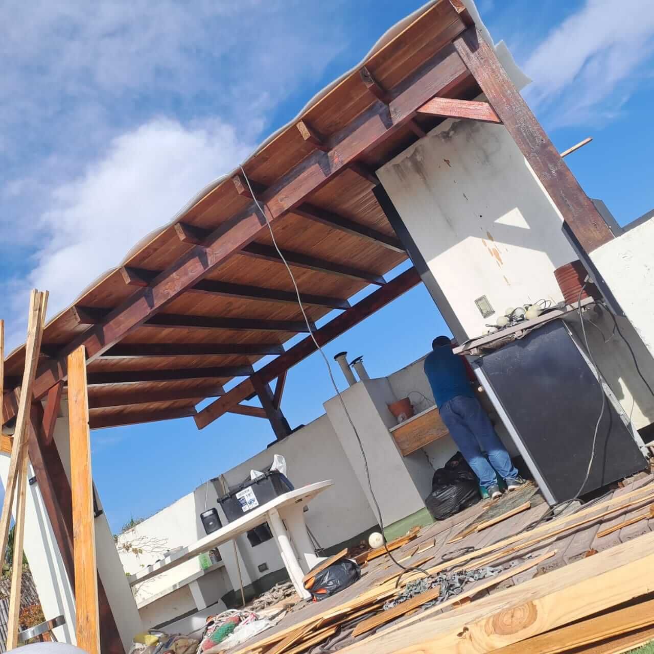Obreros colocando el techo de una casa en construcción, con vigas de madera, paredes blancas y cielo azul.