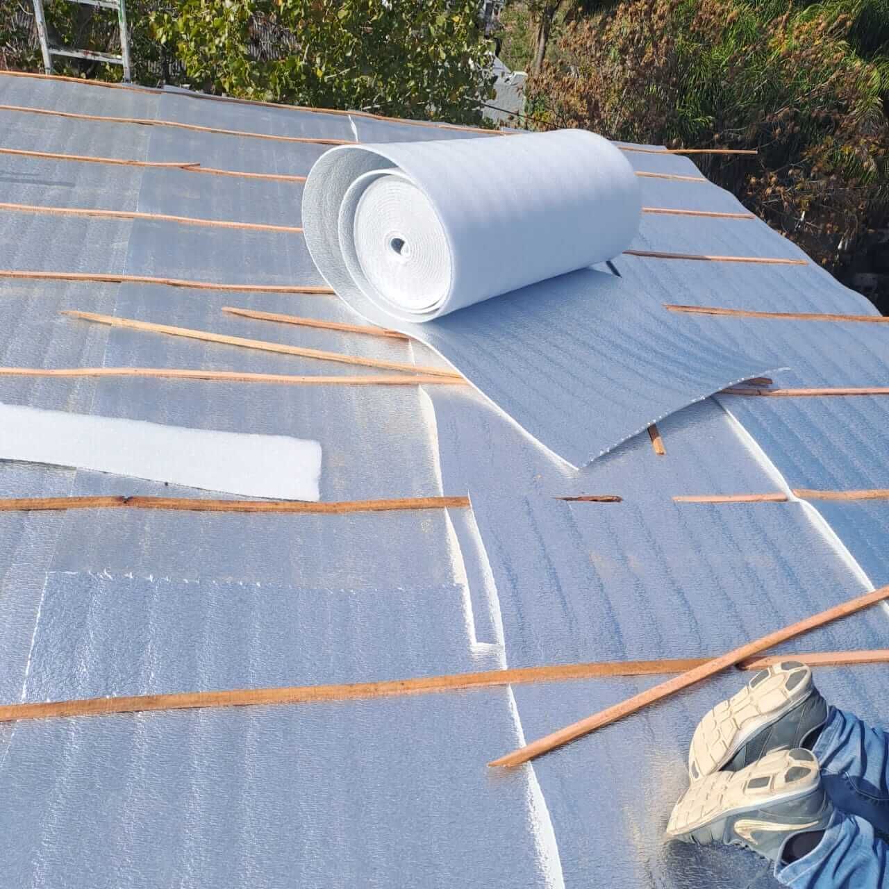 Techo en reparación con rollos de aislamiento reflectante y listones de madera colocados sobre las tejas.
