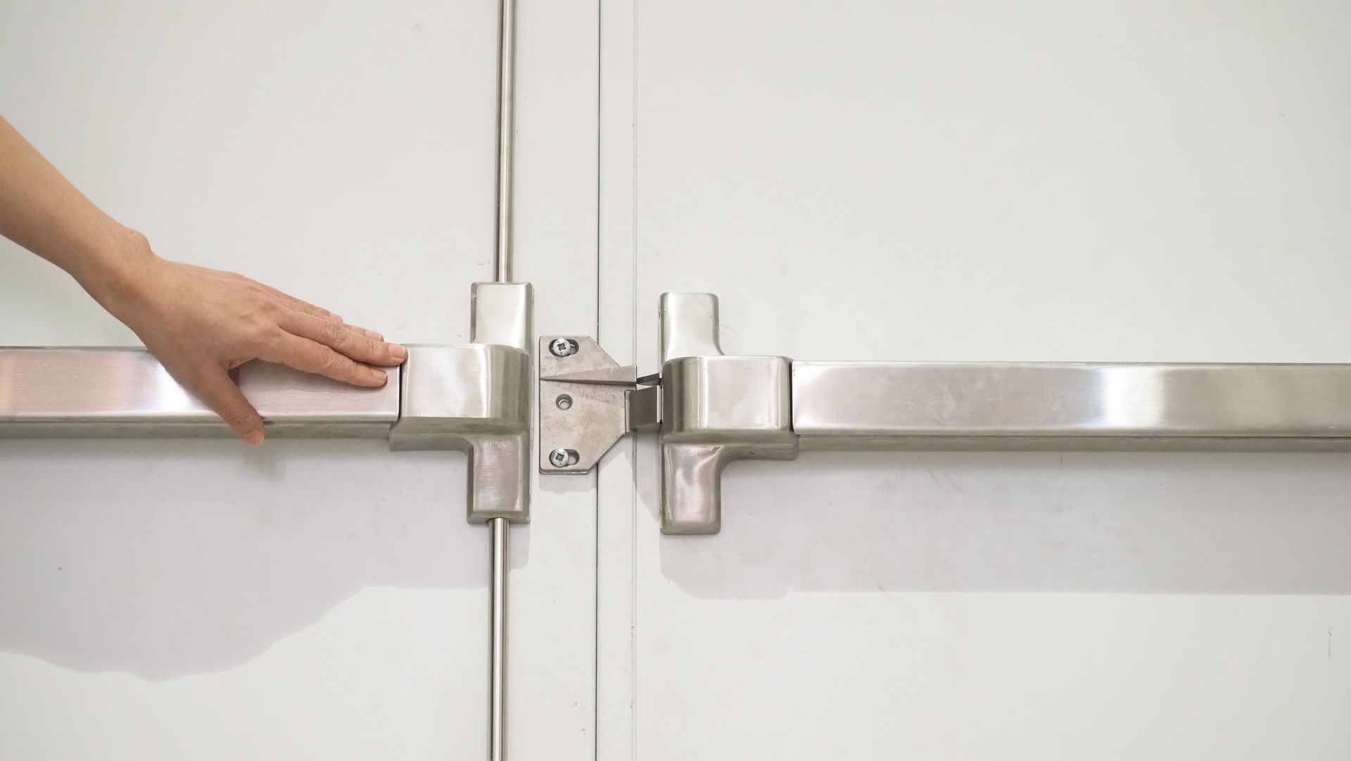 Hand securing a silver metal door latch on white double doors
