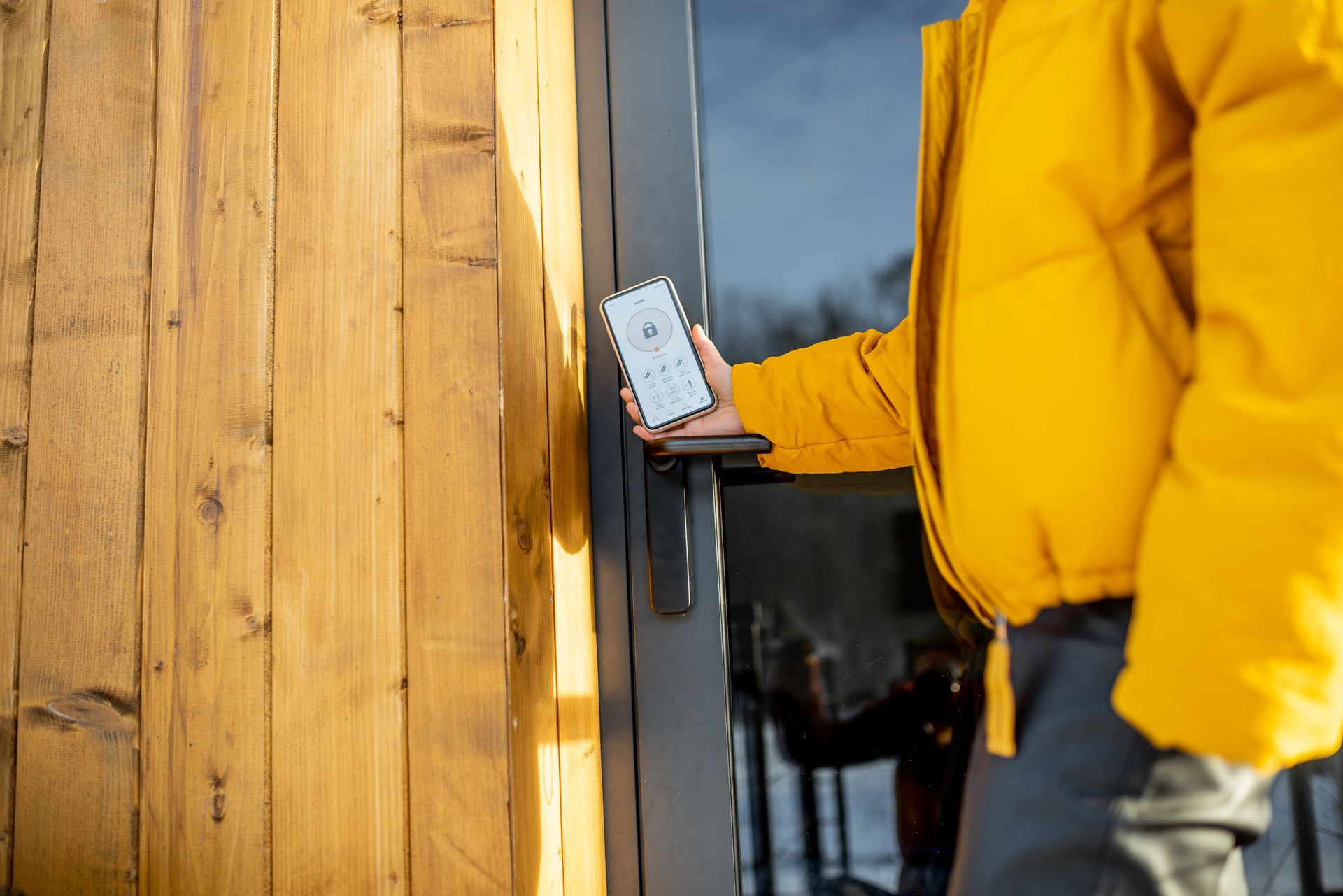 Person in a yellow jacket using a smartphone at a wooden door outdoors