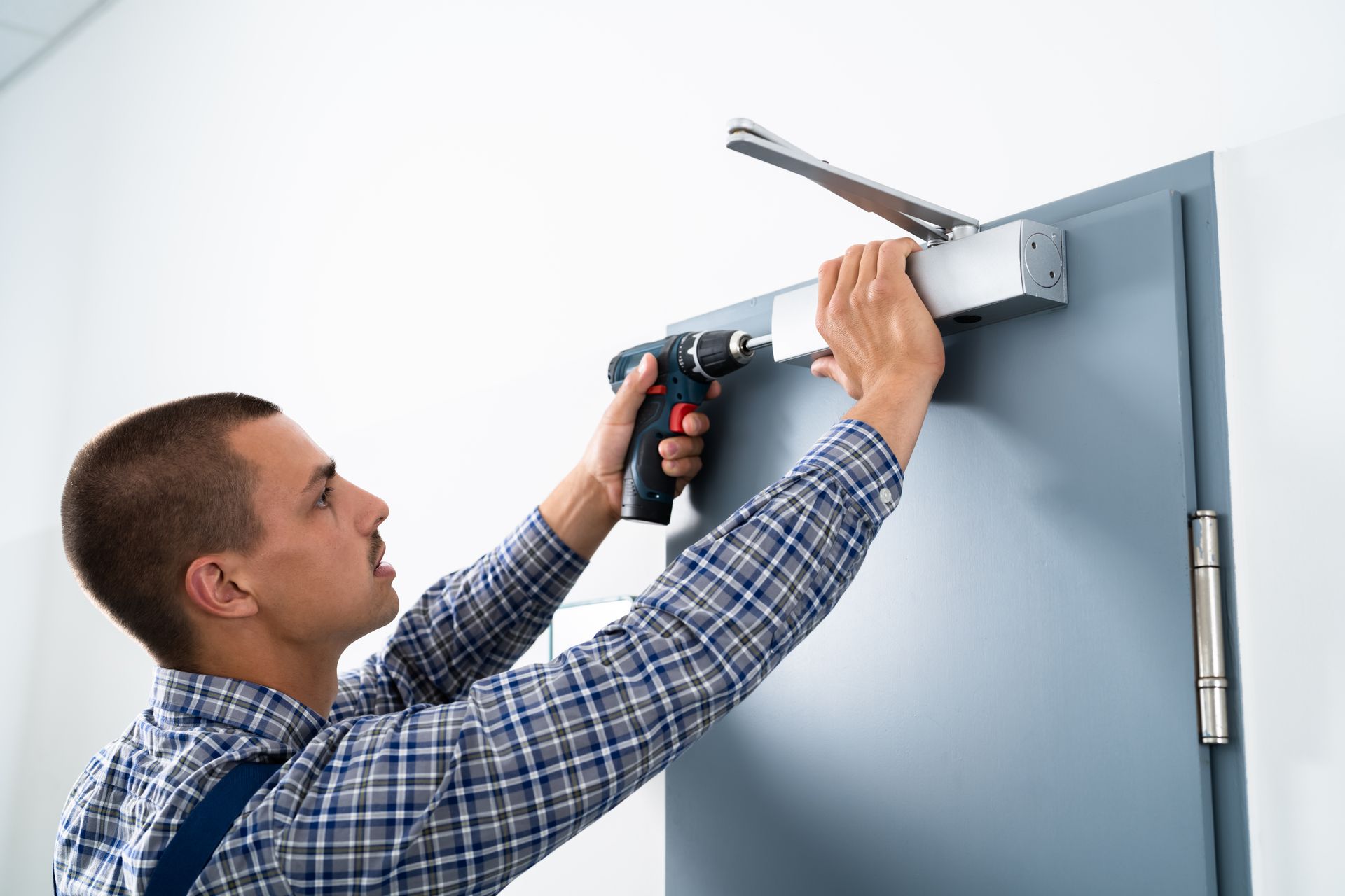 Man drilling a door closer onto a gray door with a power drill