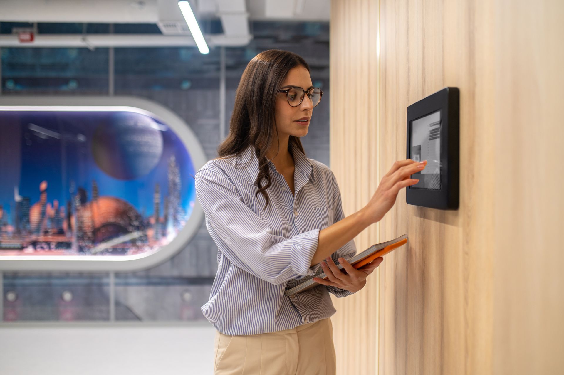a woman is holding a tablet and pressing a button on a wall .