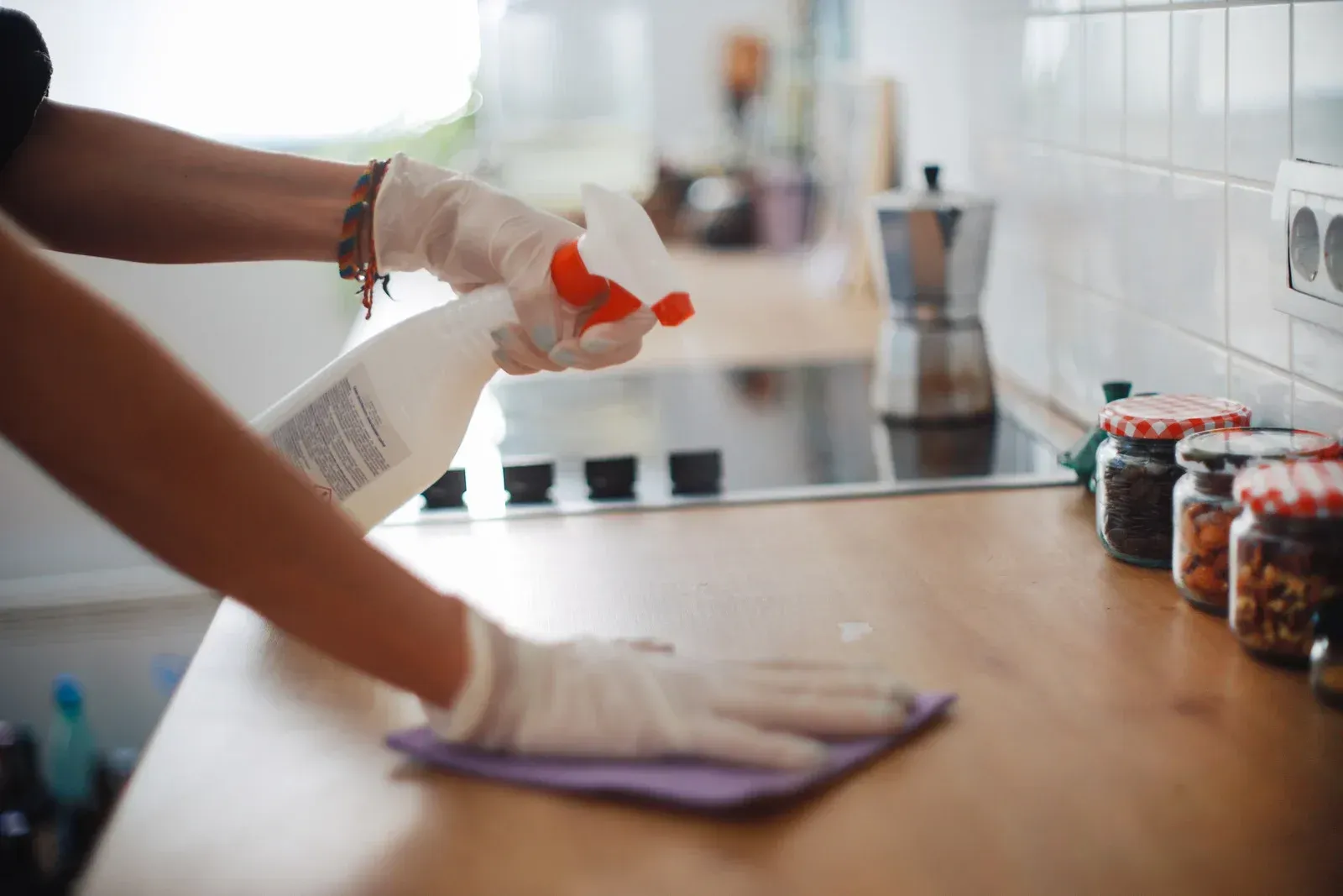 Person in gloves spraying and wiping a kitchen countertop.