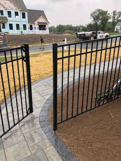 Jesse James Hardscaping - Image -Black metal fence with gate on a paver walkway. Construction site in the background.