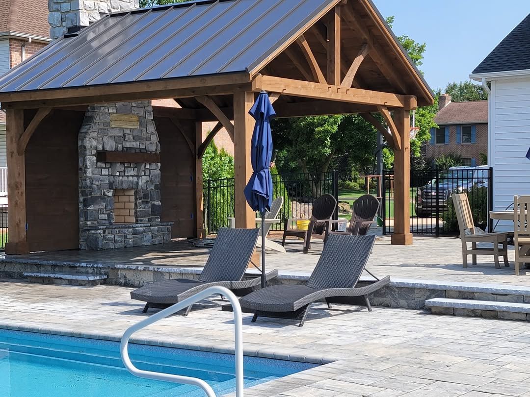 Jesse James Hardscaping - Poolside gazebo with fireplace, lounge chairs, and umbrella.
