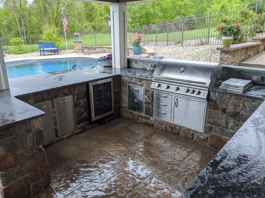 Jesse James Landscaping - Outdoor kitchen with stainless steel grill, stone facade, near a pool.