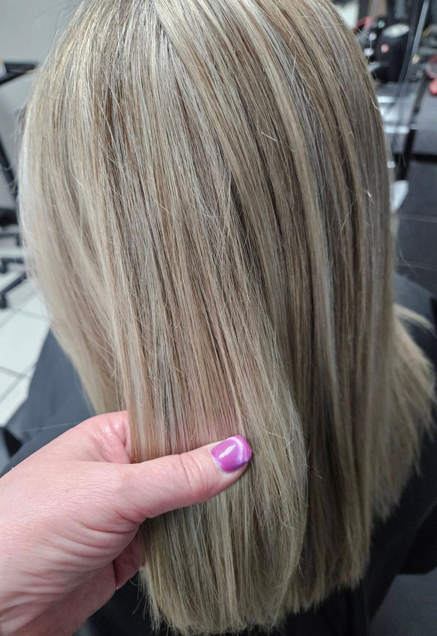 Blonde highlighted hair seen from behind, held by a hand with pink nail polish