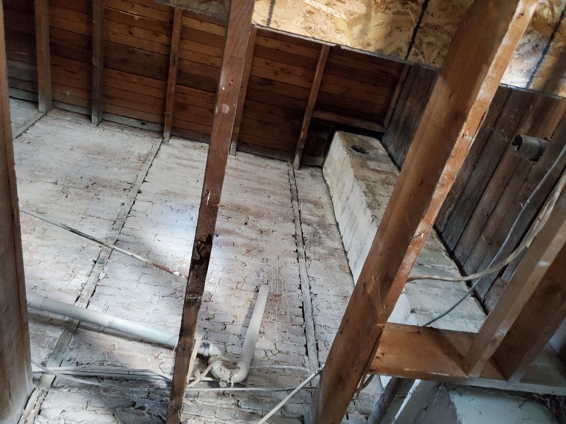 Vue intérieure d'un grenier avec poutres en bois et cheminée en béton.