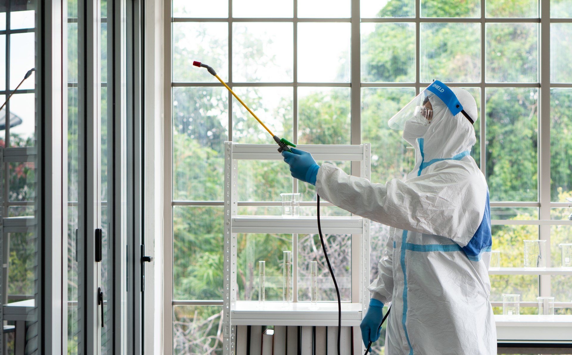 A man in a protective suit is spraying a window with a sprayer.