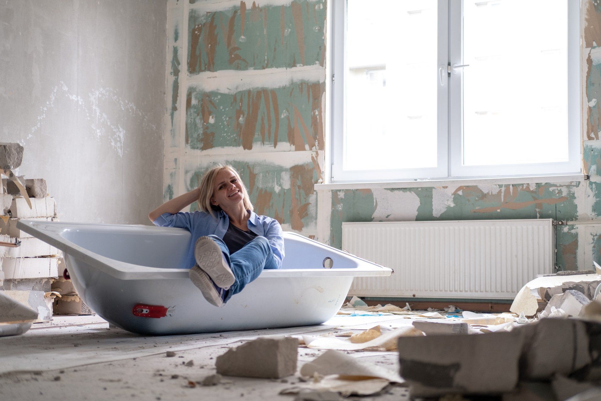 A woman is sitting in a bathtub in a room under construction.