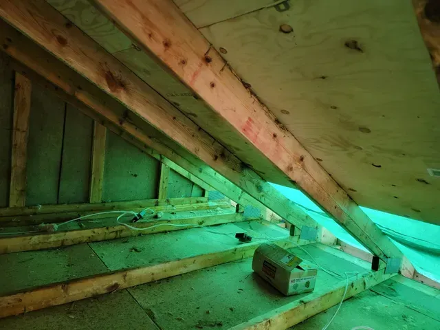 Vue intérieure d'un grenier inachevé avec poutres en bois et isolation visibles.
