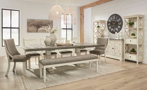 Dining room with a light wood table, chairs, and a bench, accented by white cabinets and a large clock.