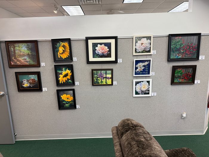 A wall displays framed floral paintings on a wall. The paintings feature sunflowers, roses, and other flowers in a variety of styles and colors.