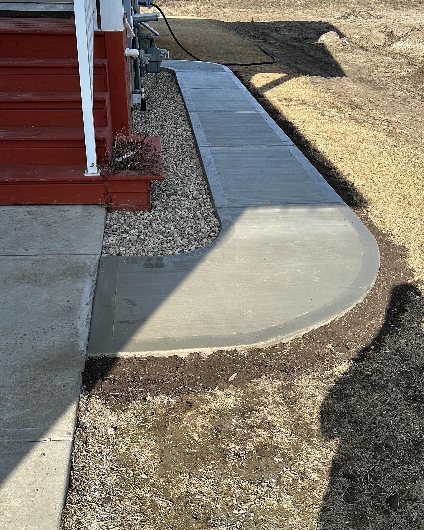 Concrete accessibility ramp beside a red building, bordered by gravel and dirt.