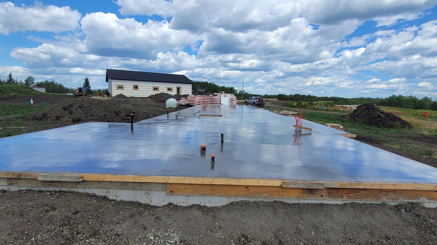 Concrete foundation slab under construction with workers and a cloudy sky in the background