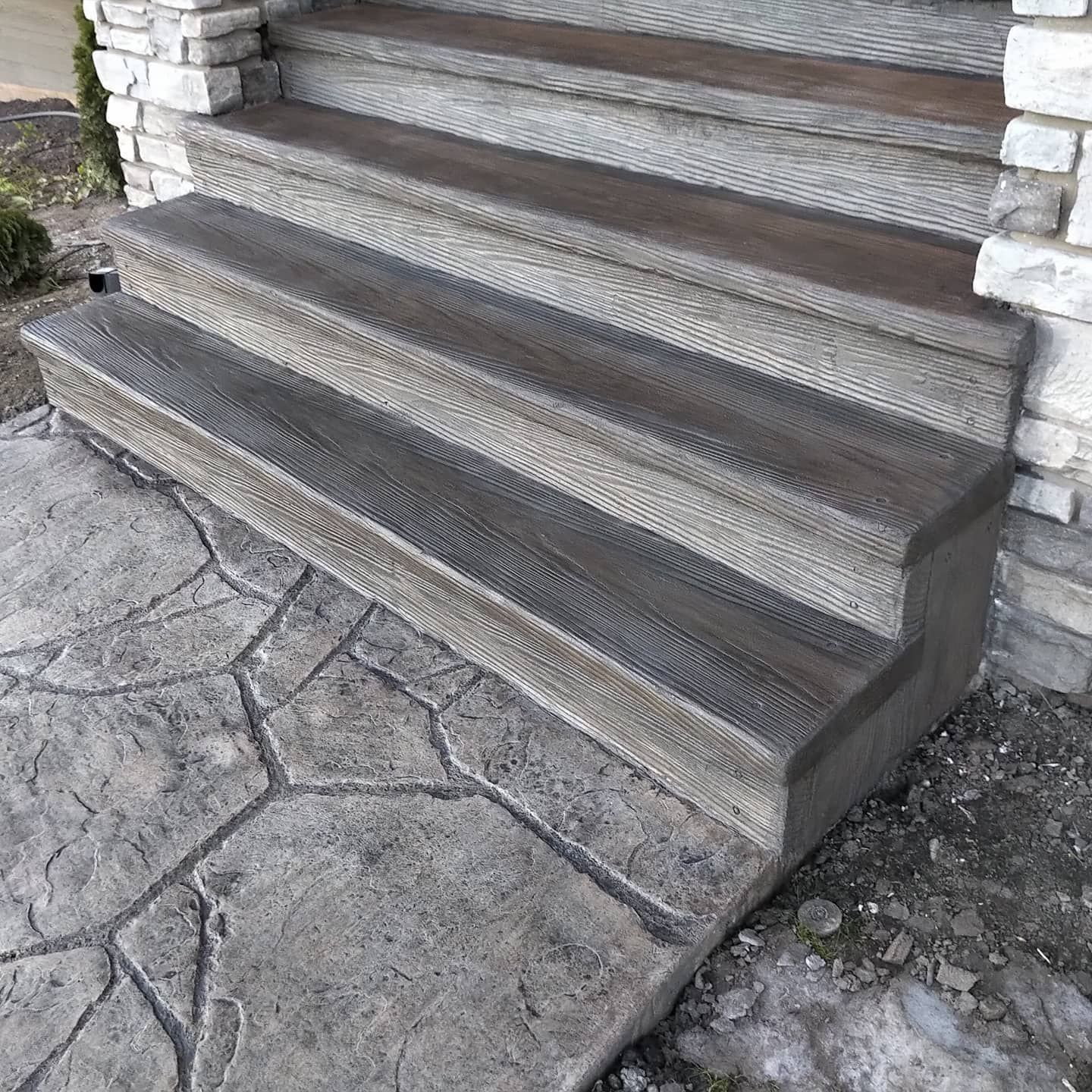 Wooden steps leading up to a stone porch, beside a textured stone walkway and wall