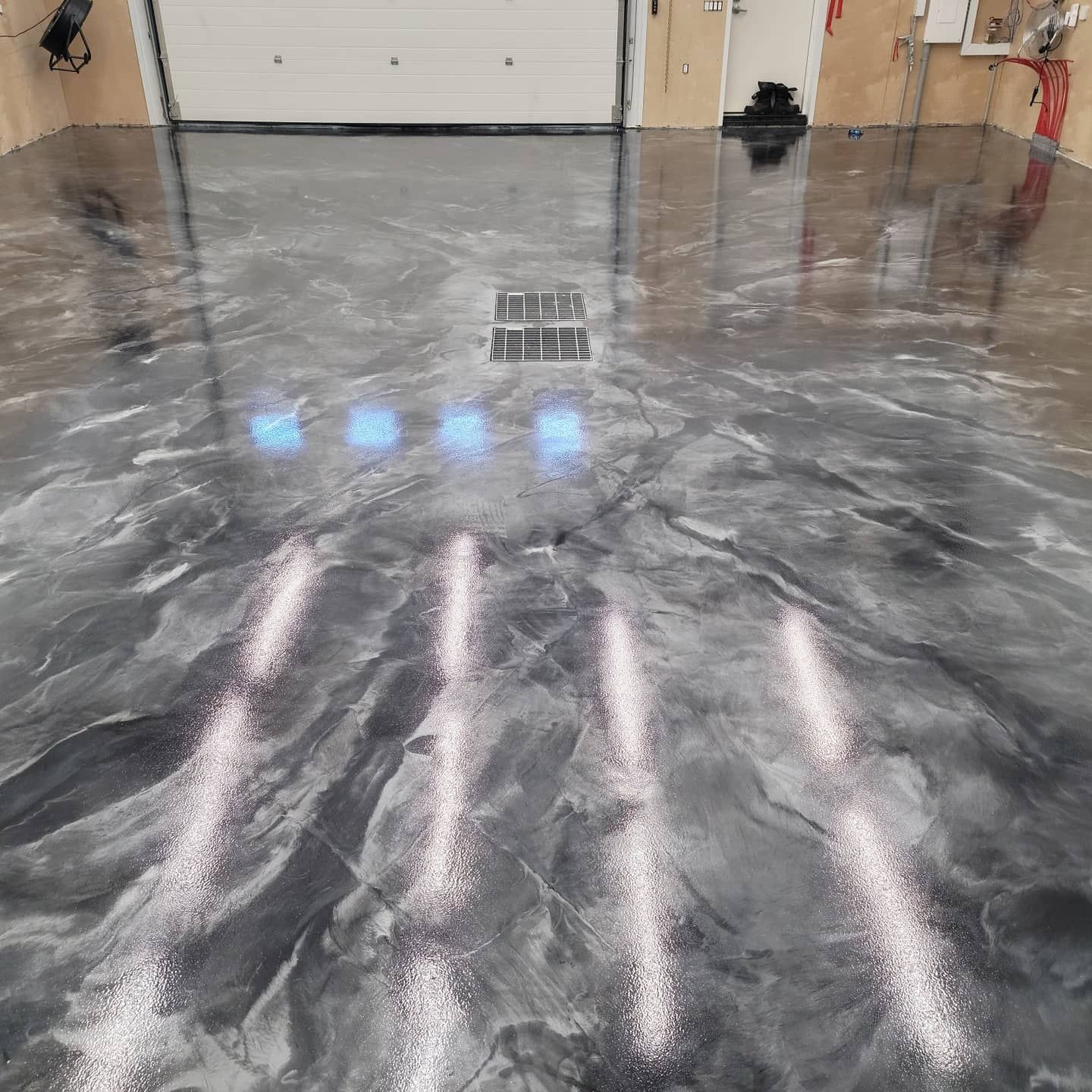 Glossy gray marbled garage floor with reflected lights and a floor drain near a closed garage door