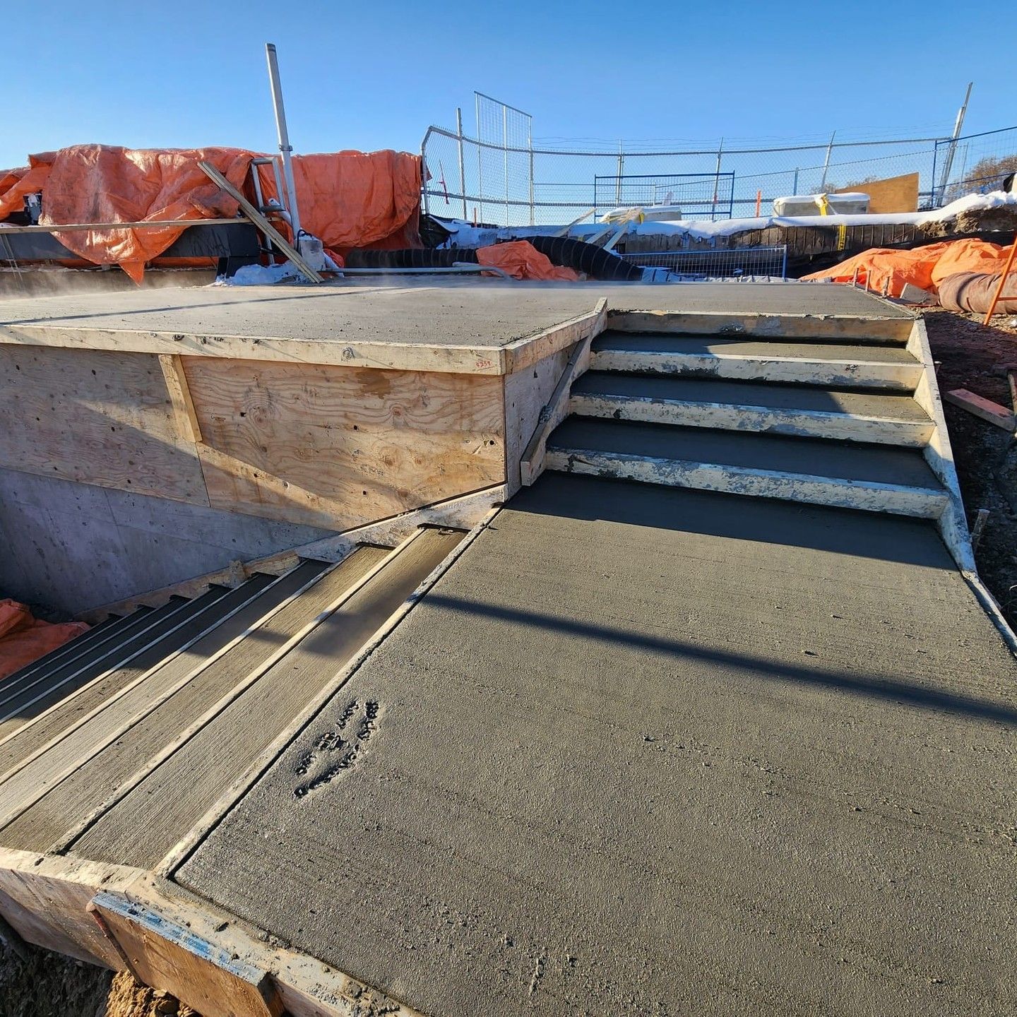 Concrete rooftop construction with stairs, orange tarps, and scaffolding under a clear blue sky
