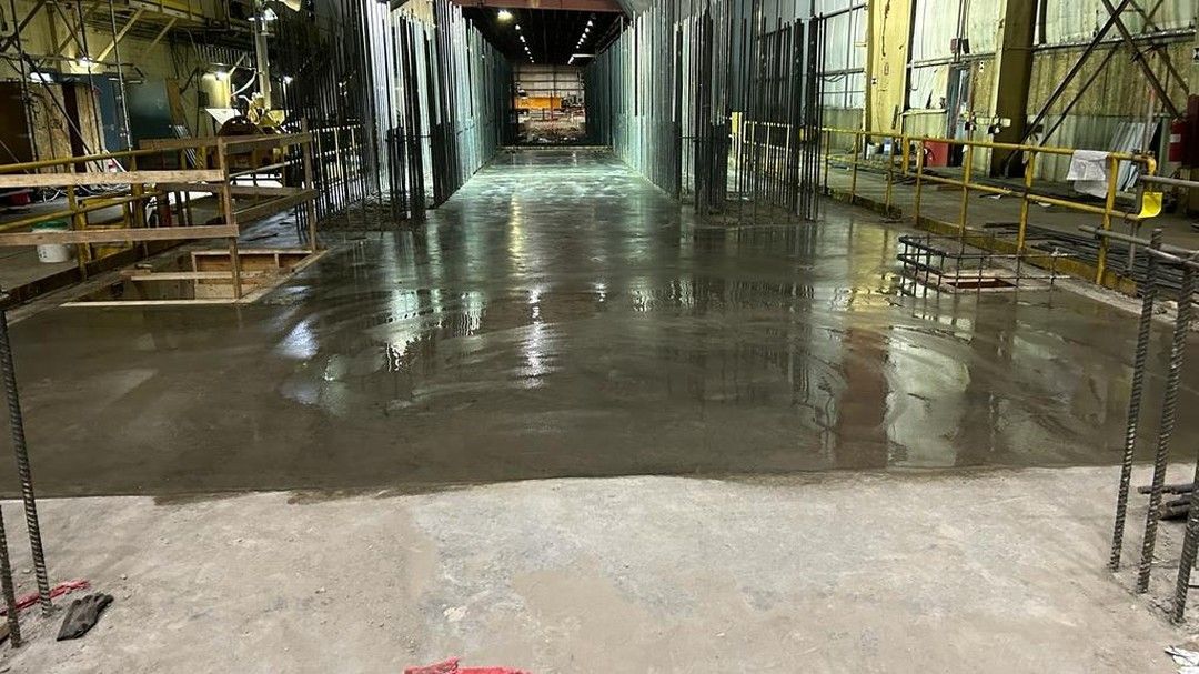 Freshly poured wet concrete floor in an industrial warehouse, reflecting overhead lights