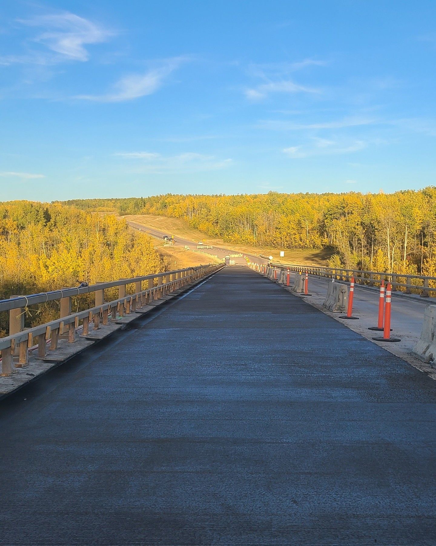New paved road bridge leading through autumn trees under a blue sky