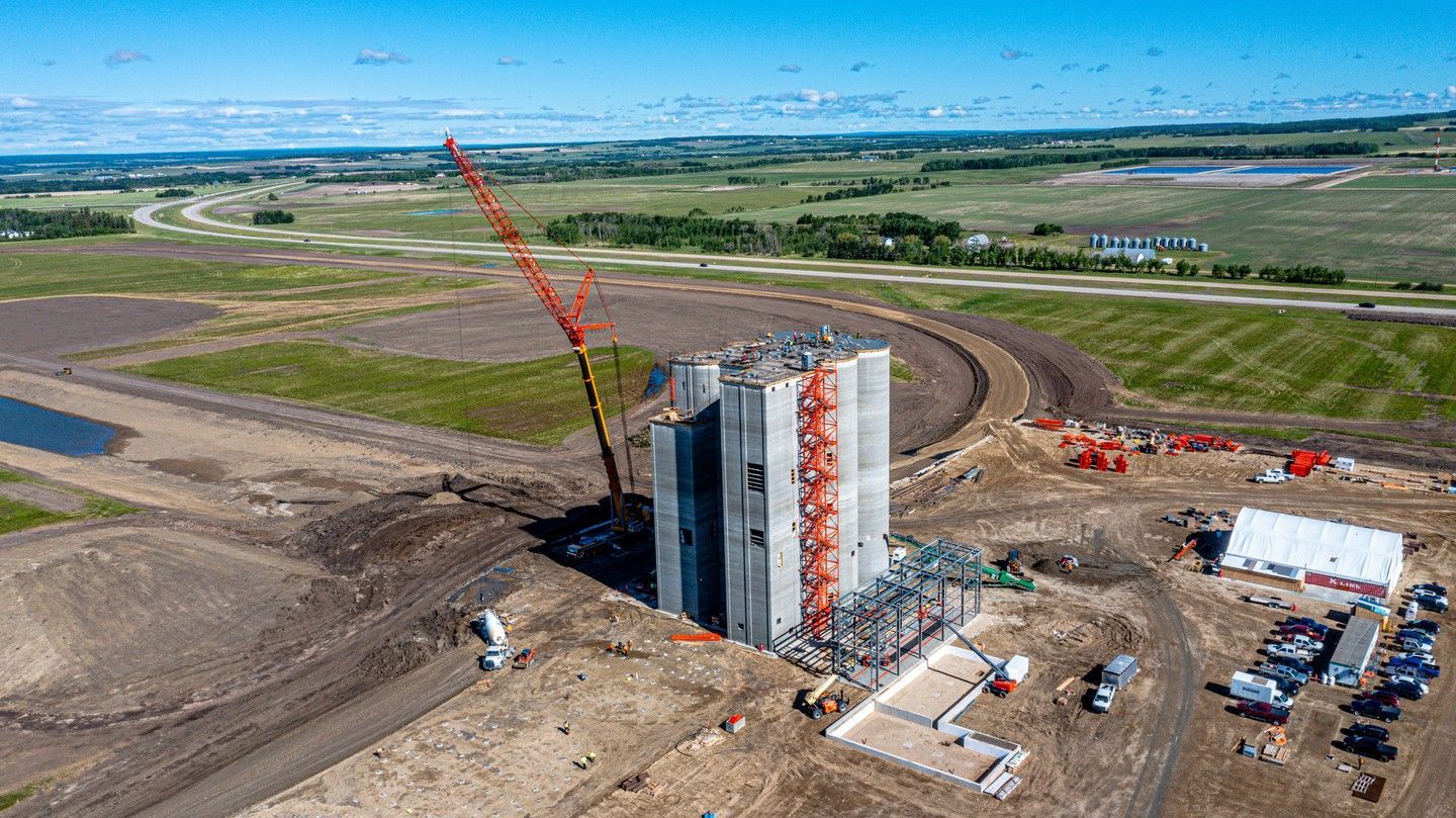 Aerial view of a construction site with a tall concrete structure, crane, and earthmoving equipment.