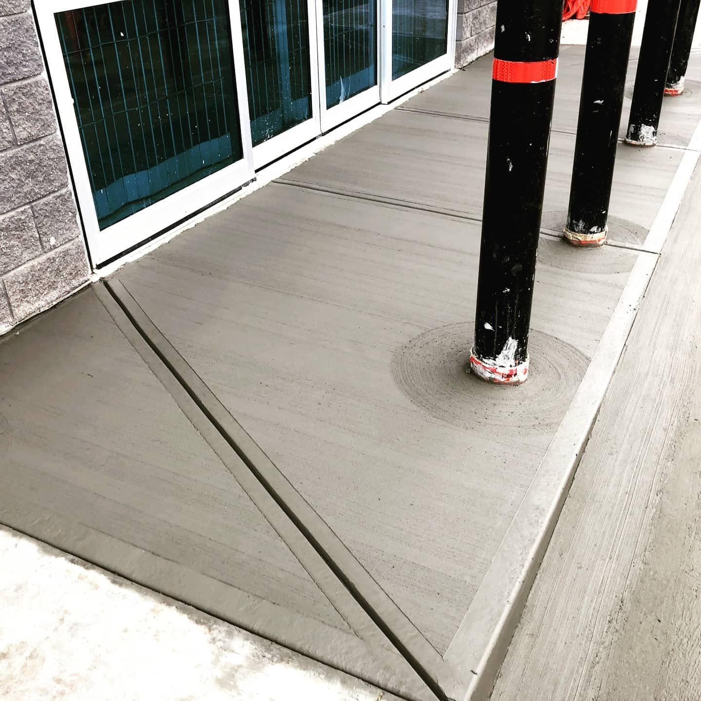 Concrete sidewalk ramp with black-and-red poles beside glass storefront windows