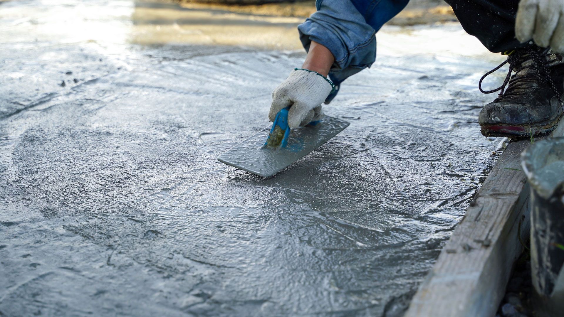 Worker smoothing wet concrete with a trowel at a construction site