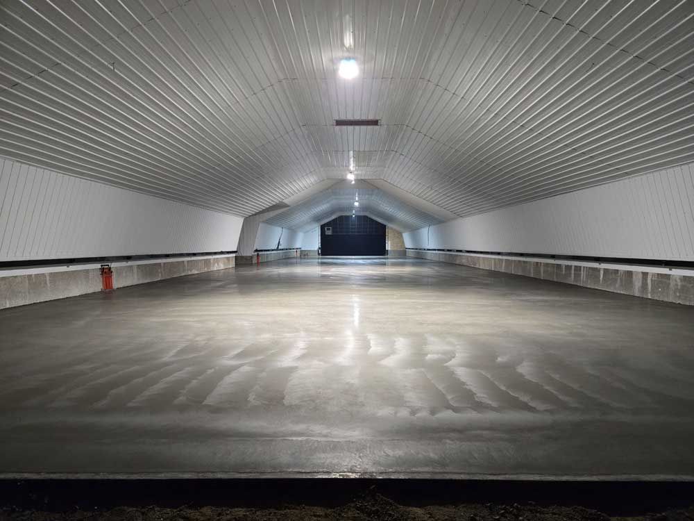 Empty arched tunnel with white walls and a wet concrete floor, lit by overhead lights
