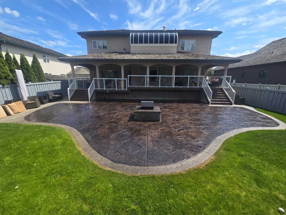 Two-story house with a large covered patio and curved dark stone patio, bordered by a green lawn.
