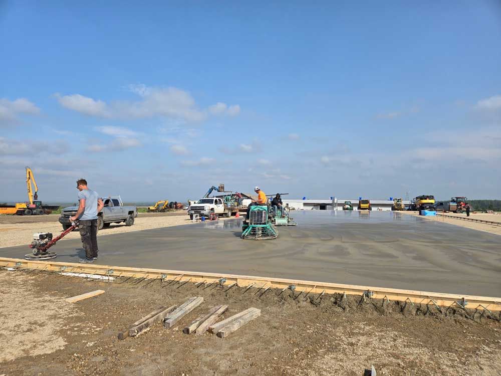 Workers and construction vehicles paving a large concrete slab under a blue sky