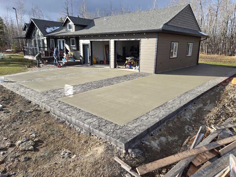Single-story house with a large concrete patio and stone border under construction or renovation.
